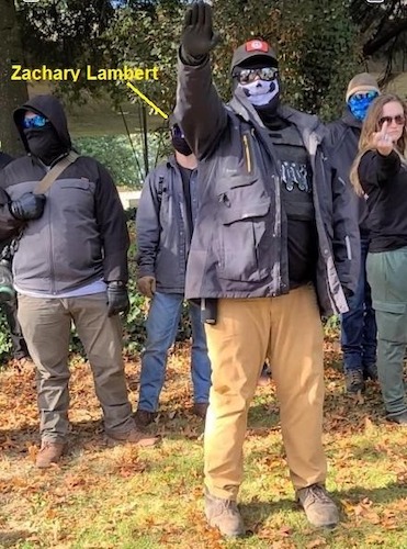 Neo-Nazi Zachary Lambert at a transphobic, anti-LGBTQ rally in Eugene protesting a childrens drag story hour. In front of him, another member of his group performs a sieg heil for the camera.