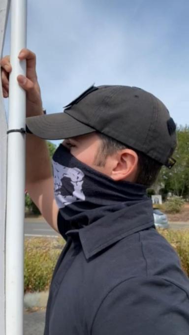 Neo-Nazi Zachary Lambert wearing a skull mask and holding a banner that says "gender theory is poison".