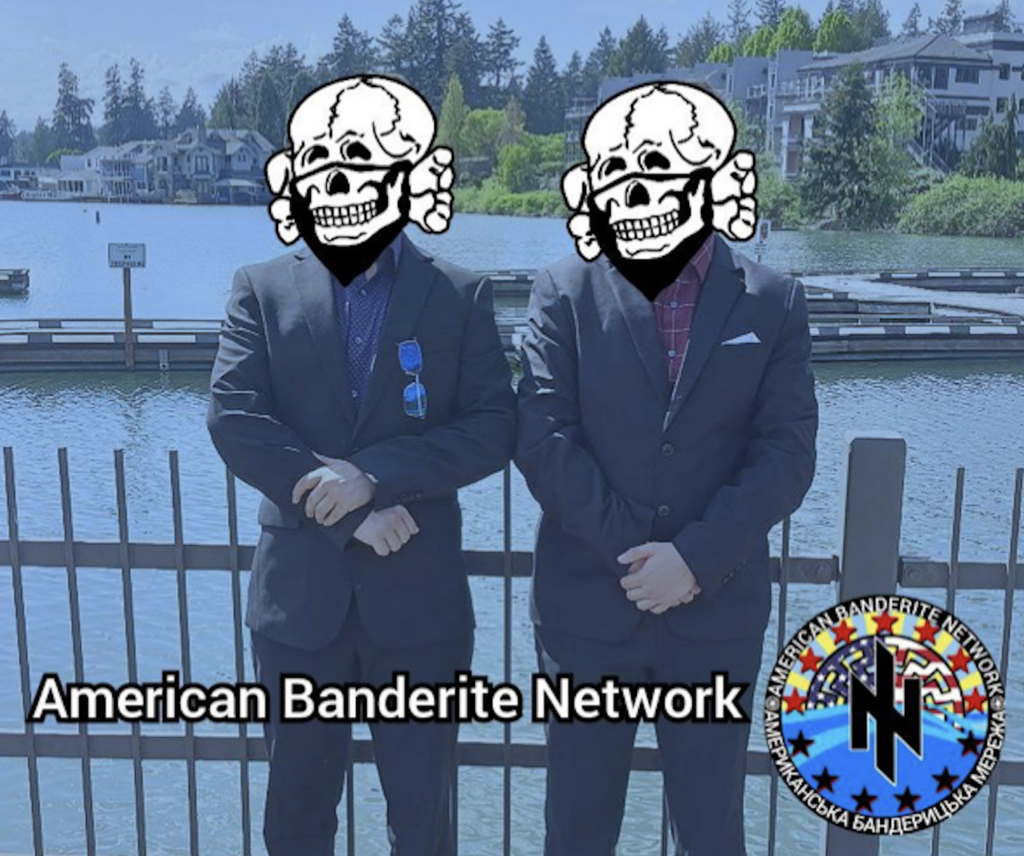 two young men stand next to each other wearing suits in Lake Oswego, Oregon. There is a metal fence and lake behind them. They have totenkopfs covering their faces to conceal their identities. There is an American Banderite Network logo on the photo.