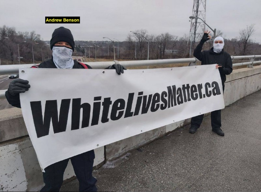 Andrew Benson and a second man stand on a freeway overpass holding a banner that reads "WhiteLivesMatter.ca."