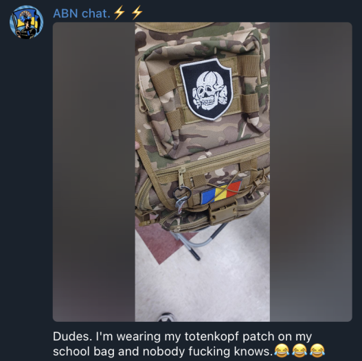 screenshot from ABN chat that shows a backpack with totenkopf patch on it, which features a skull and crossbones. There is a Romanian flag patch on the backpack also. The text below the photo says “Dudes. Im wearing my totenkopf patch on my school bag and nobody fucking knows” followed by three laughing emojis. 
