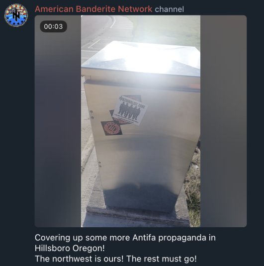 a screenshot from the ABN telegram channel showing nazi stickers being placed on a silver box outdoors. The text reads “covering up some more antifa propaganda in Hillsboro Oregon! The northwest is ours! The rest must go!”
