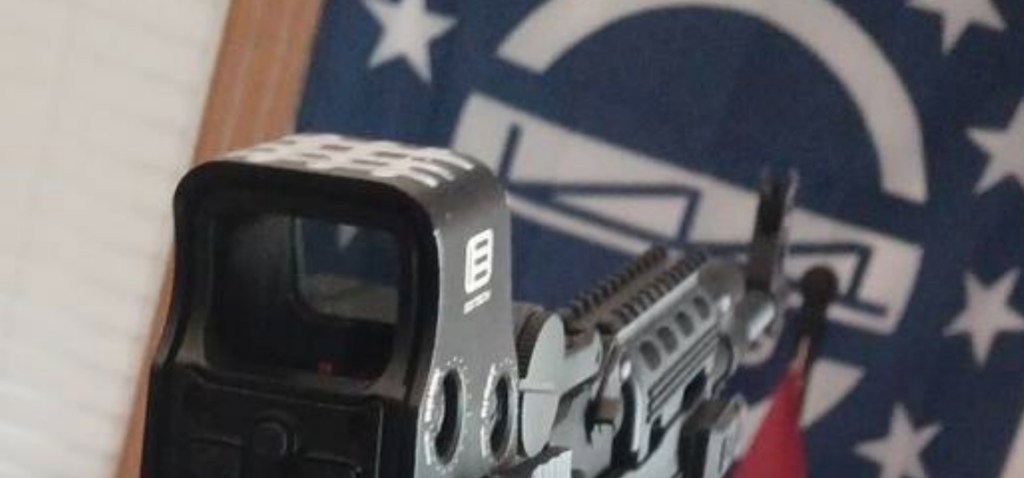 Close up picture of the optic on top of a rifle. There is a St.Michael's Cross drawn on to the top of the optic. 
